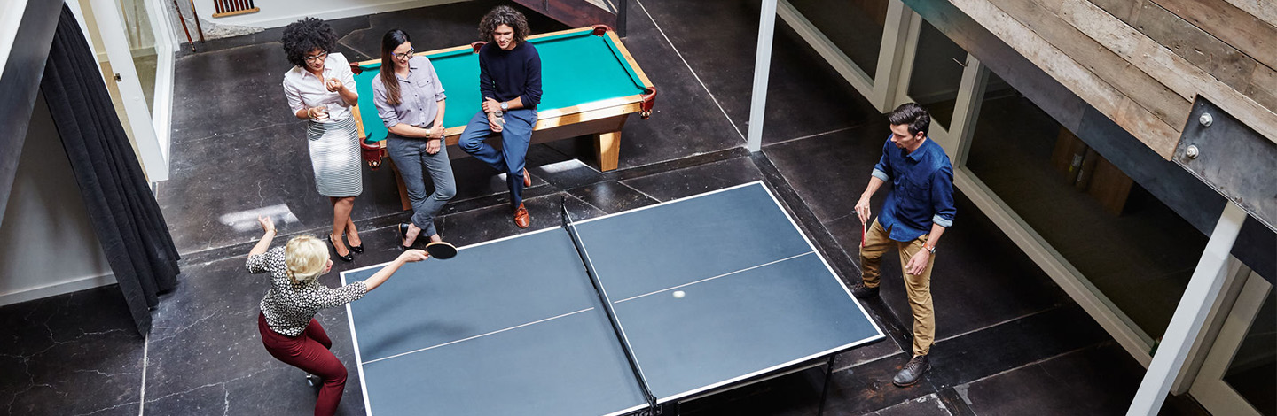 A group of employees gathered around and playing ping pong