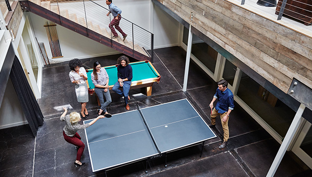 A group of employees gathered around and playing ping pong