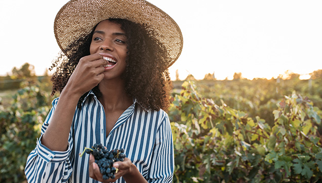 A woman eating grapes in a vineyard