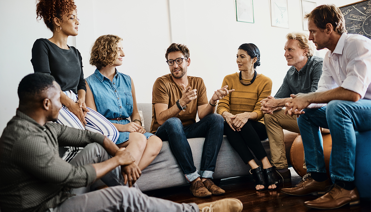 A group of employees sitting around a couch listening to one person talk
