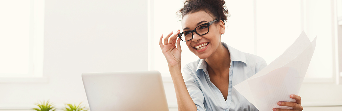 A woman holding papers at a desk and smiling