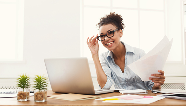 A woman holding papers at a desk and smiling