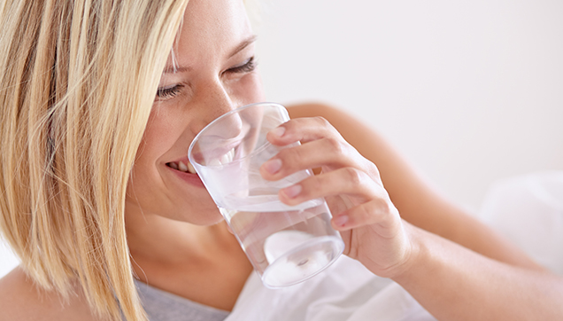 A woman drinking a class of water in bed