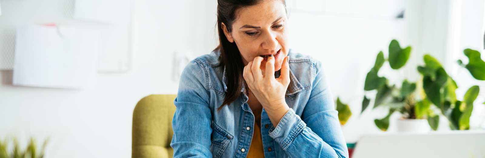 A woman sitting at a desk and biting her fingernails