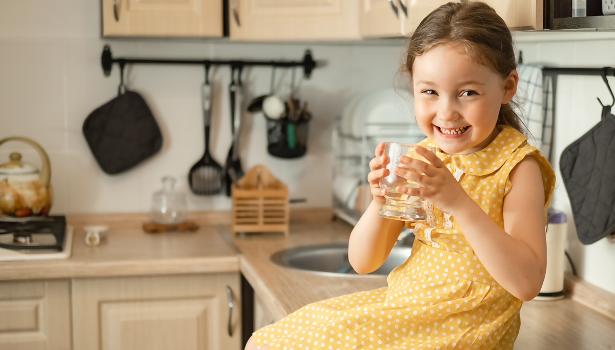 A girl drinking a glass of water in a kitchen