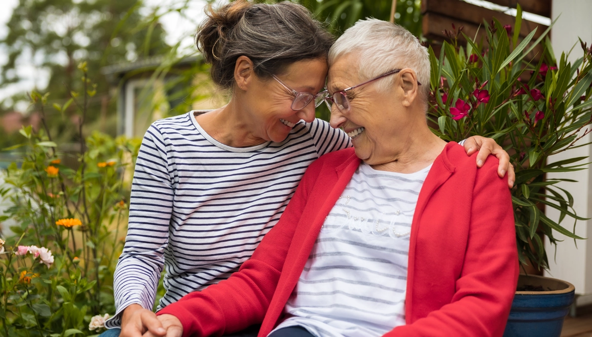 A daughter and older mother sitting in a garden and laughing