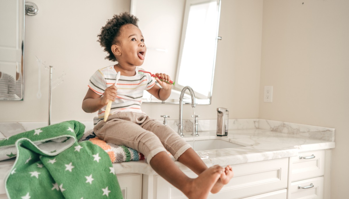 A child sitting on a sink and brushing their teeth