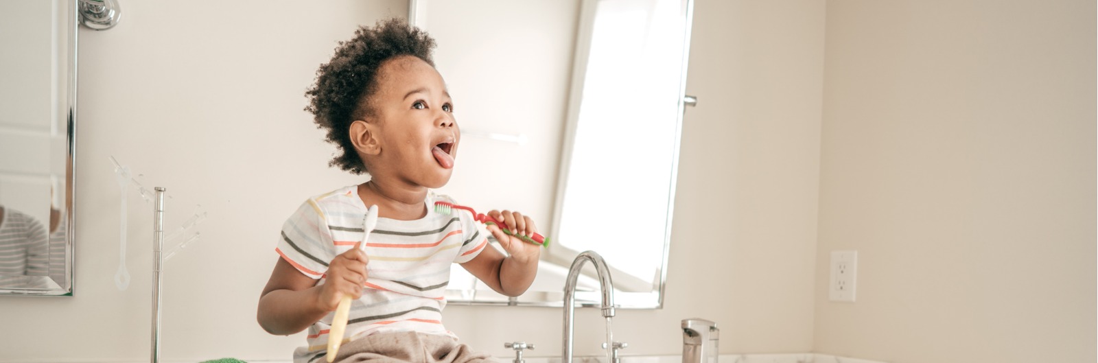 A child sitting on a sink and brushing their teeth