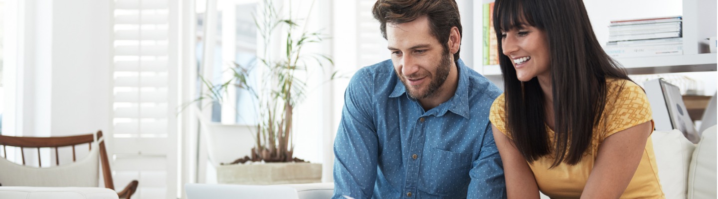 A couple is smiling while looking at a laptop together.