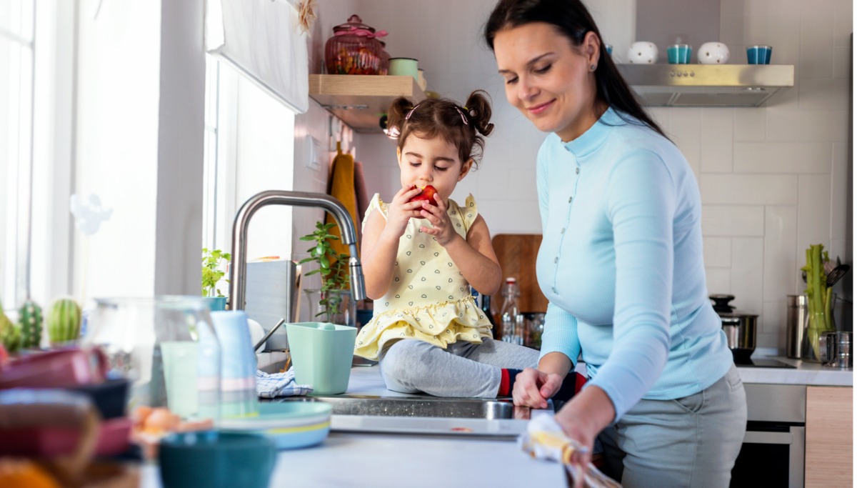 A mother and child eating an apple at the kitchen sink