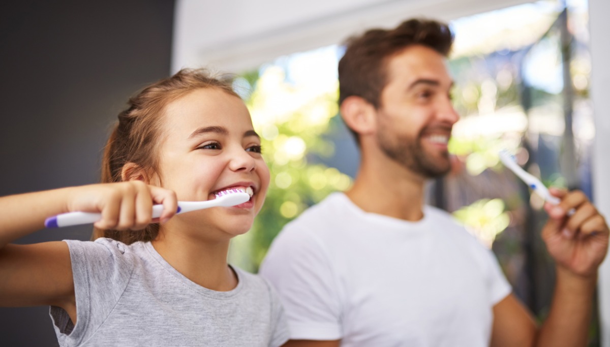 A dad and daughter brushing their teeth