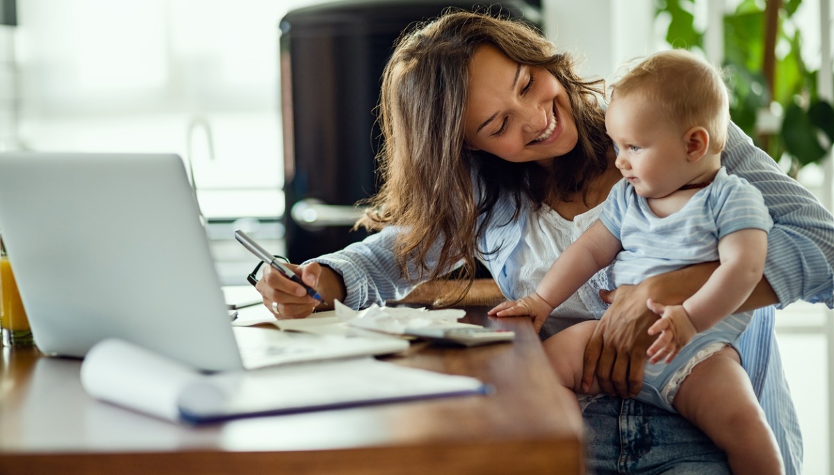 A mother and baby sitting at a desk looking at laptop