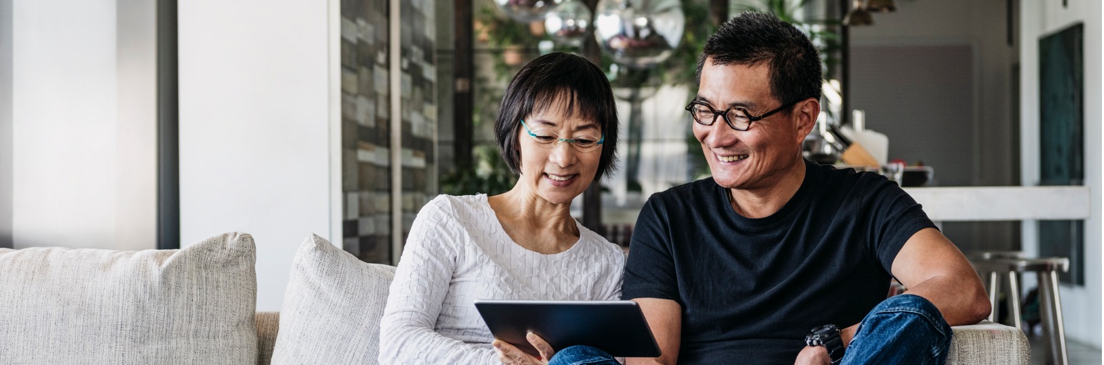 A couple sitting on a couch looking at a tablet device.