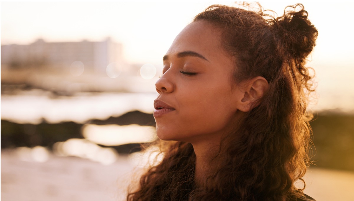 A woman breathing deeply outside with her eyes closed