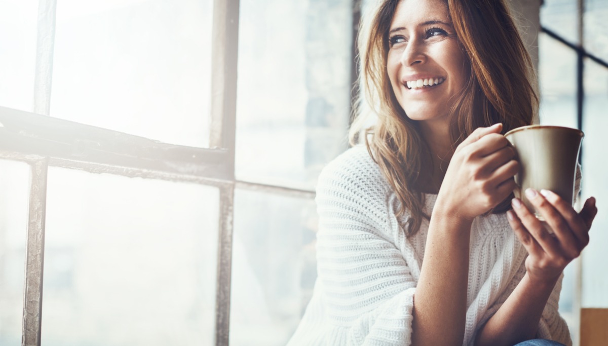 A woman drinking from a mug by a sunny window