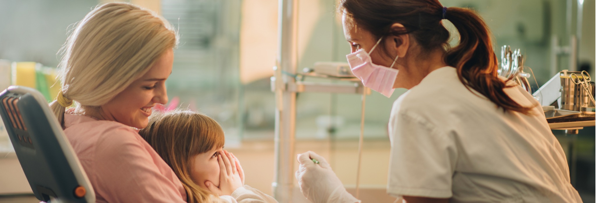 A dentist calming a young girl as she is held by her mother
