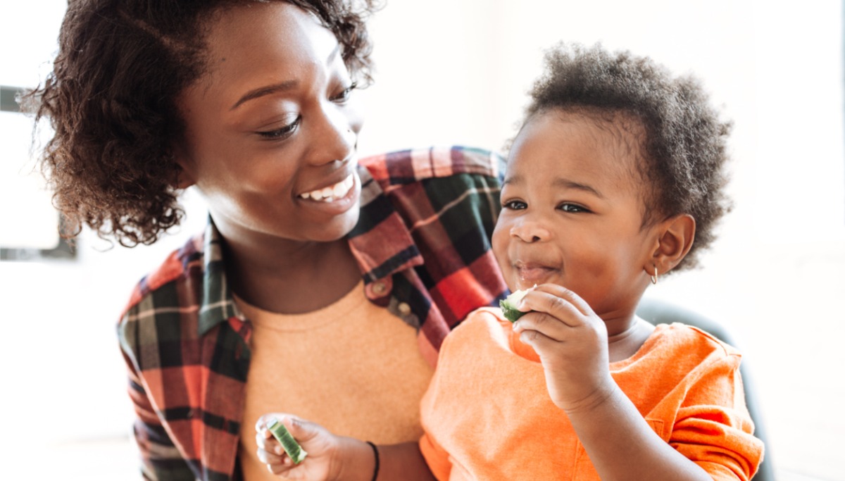 A mother and toddler smiling while eating vegetables