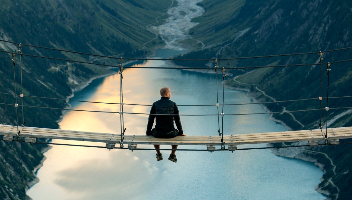 Man sitting on the edge of a bridge and pondering with a beautiful lake in the background