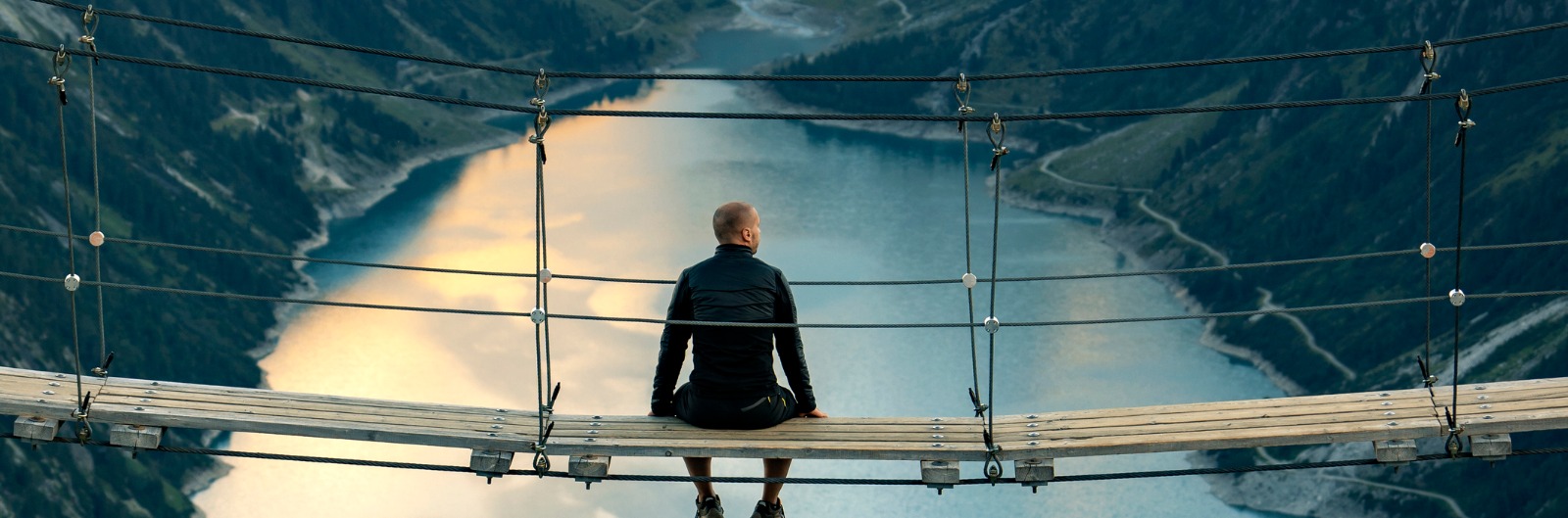 Man sitting on the edge of a bridge and pondering with a beautiful lake in the background