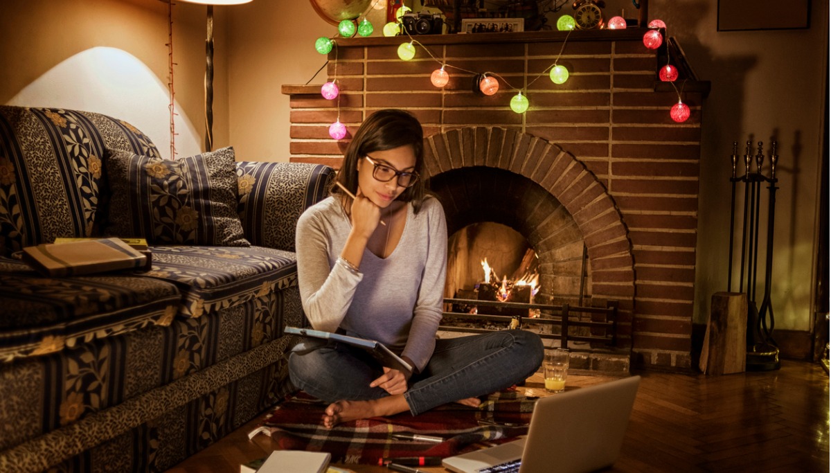 A woman sitting next to a fireplace while looking for dental insurance on a tablet device.