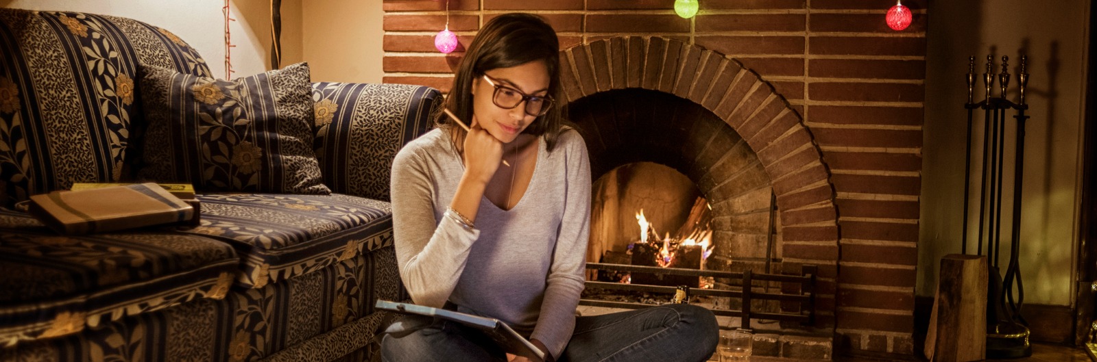 A woman sitting next to a fireplace while looking for dental insurance on a tablet device.