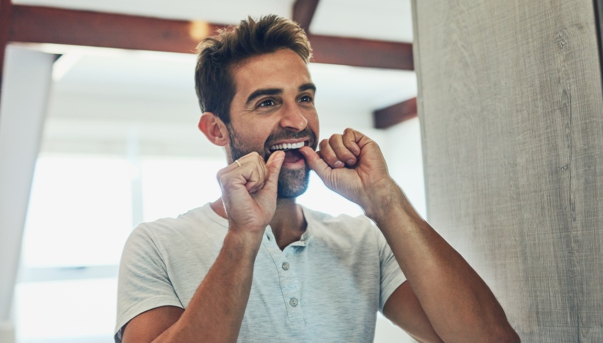 A man flossing his teeth in a mirror
