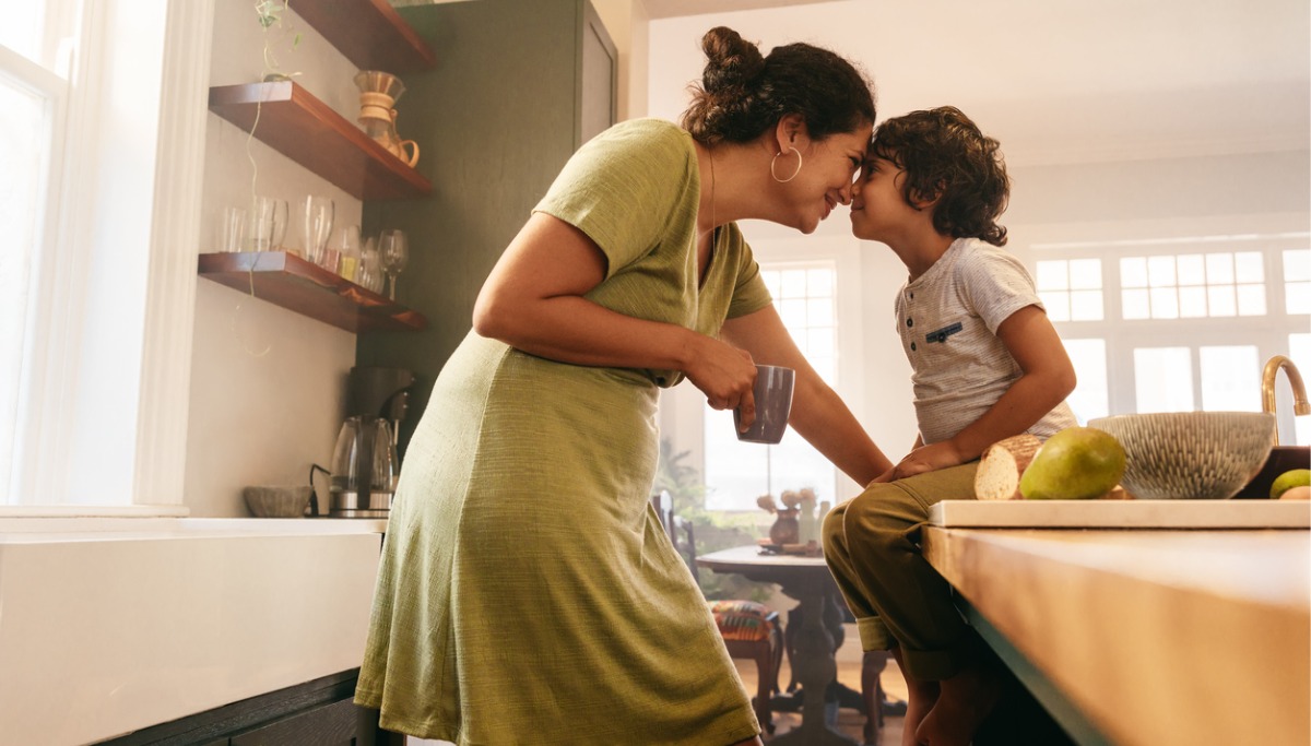 A mother and child nose to nose in a kitchen while smiling