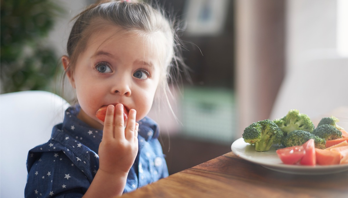 A young child eating vegetables at a kitchen table
