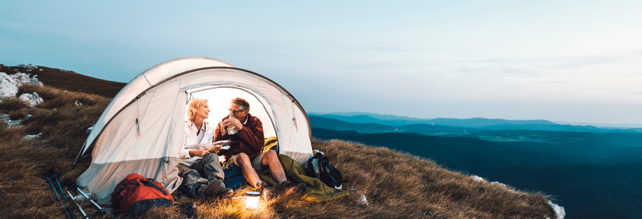 A couple sitting in a tent on a mountain top drinking from mugs