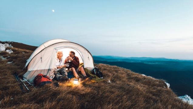 A couple sitting in a tent on a mountain top drinking from mugs