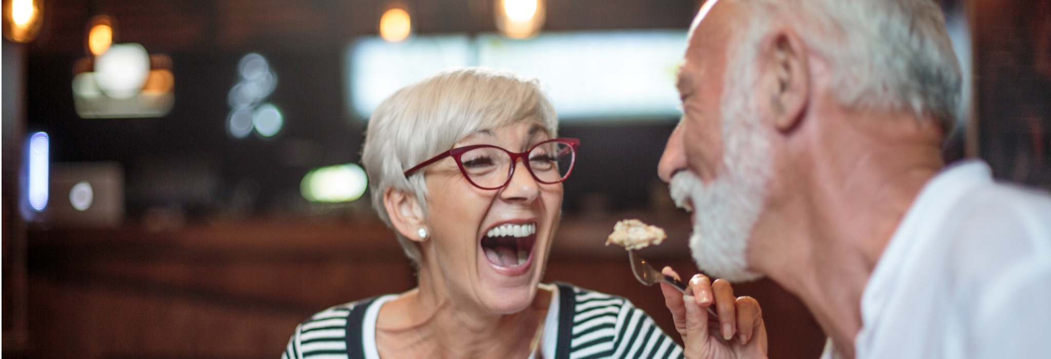 A older woman feeding food to her husband and laughing