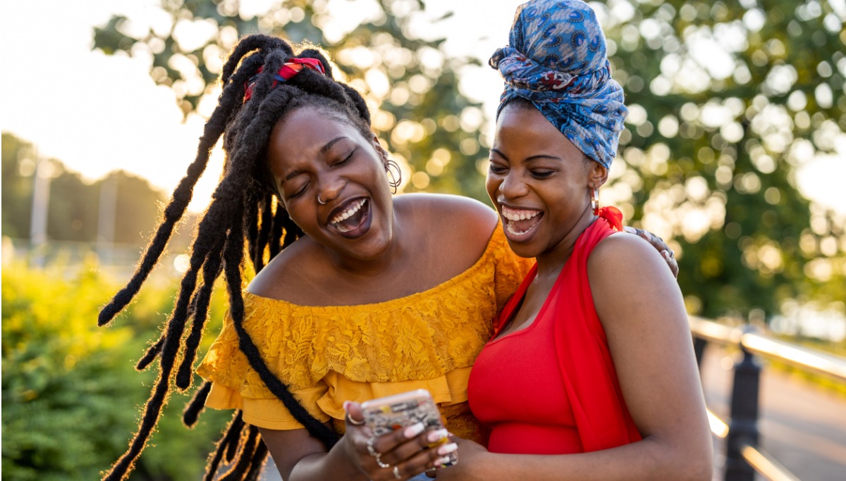 Two woman looking at their phone outside and laughing