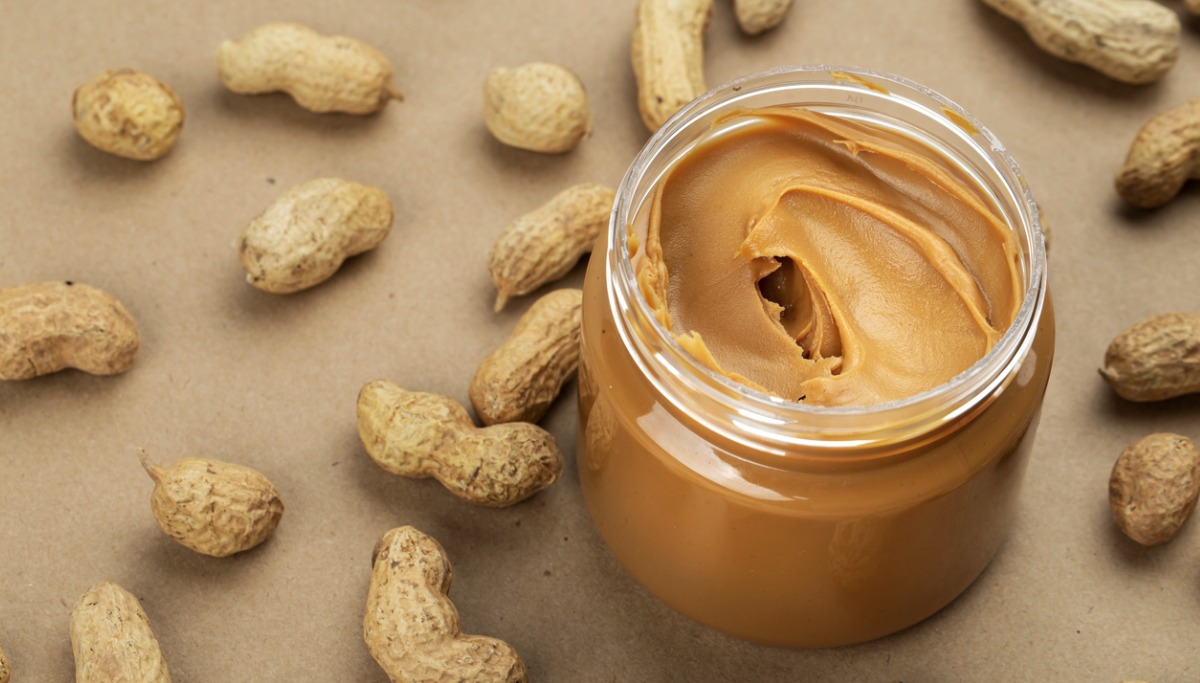 A jar of peanut butter on a table with peanuts around it