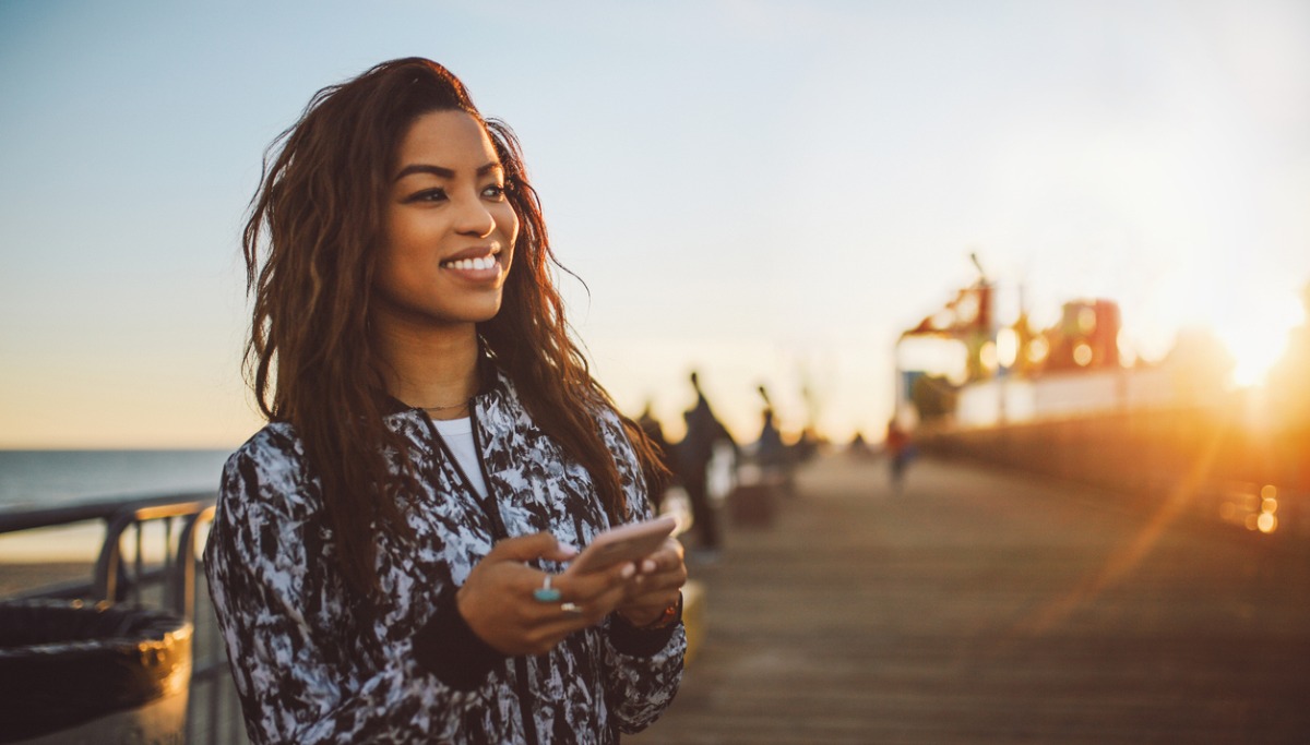A woman standing on a pier at sunset using her phone