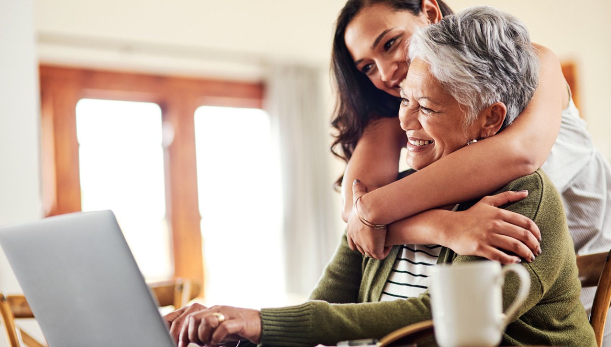 A daughter hugging her mother as they look at a laptop