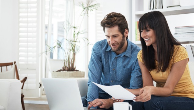A couple is smiling while looking at a laptop together.