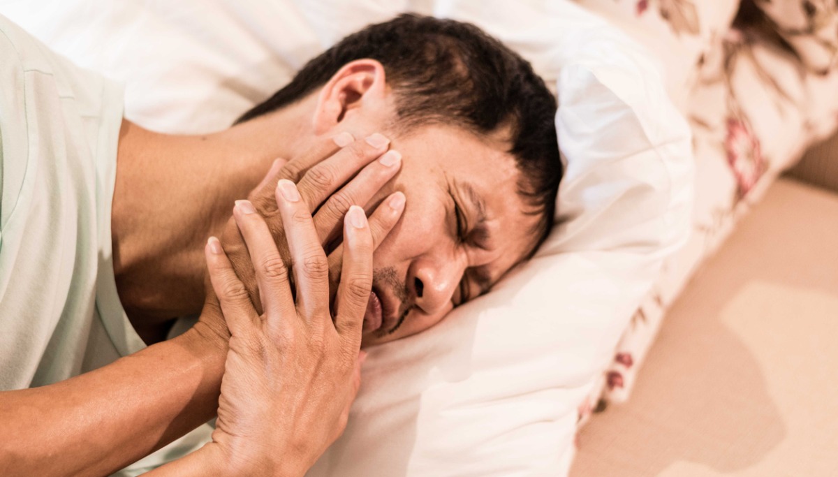 A man laying in bed holding his jaw in pain