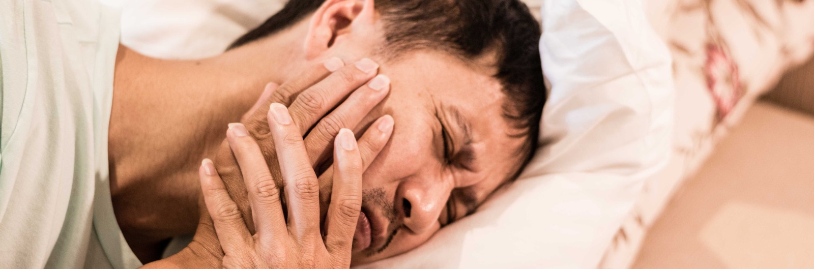 A man laying in bed holding his jaw in pain