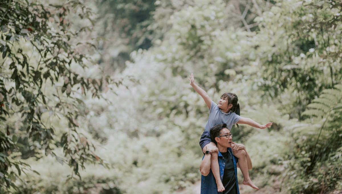 A young child in the woods sitting on her father's shoulders