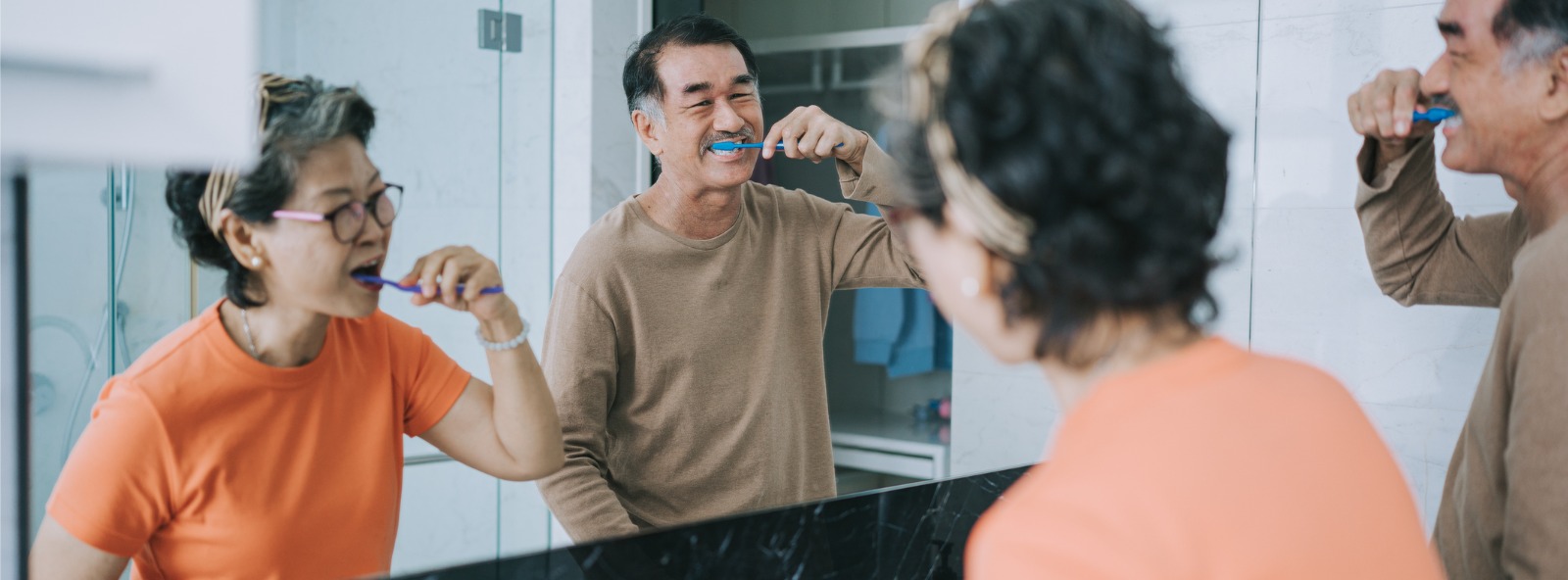 A couple brushing their teeth while looking in the mirror