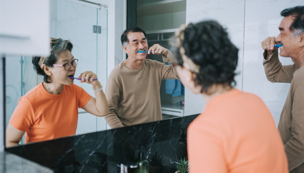 A couple brushing their teeth while looking in the mirror