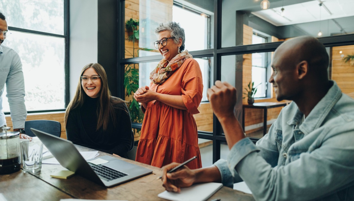 A group of employees gathered around a computer and laughing