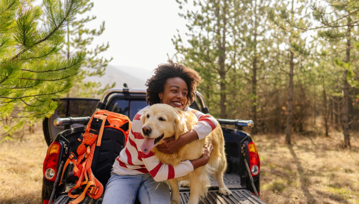 A woman sitting in the back of a pickup truck and holding a dog